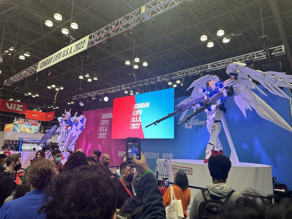 Angled photo of Gundam Expo USA 2022's event stage from Anime NYC 2022. It has two large scale models of Wing Gundam Zero and Gundam Aerial's mobile suits on both ends.